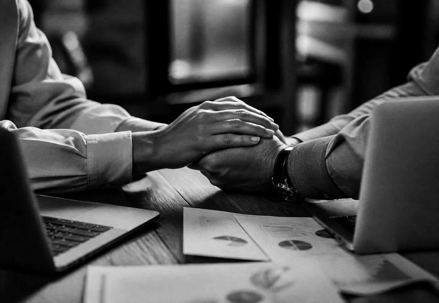 Manos de dos personas sobre una mesa con portátiles y gráficos impresos